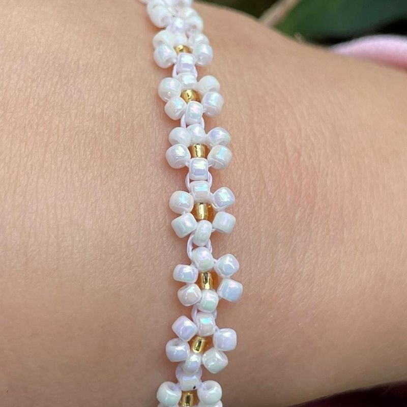 Close-up of a white beaded bracelet with gold accents on a wrist.