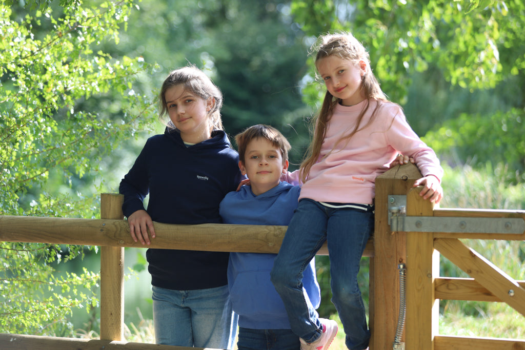 Three children sitting on a wooden fence with a natural background